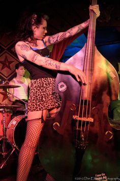 a woman in fishnet stockings playing the bass on stage with other musicians behind her