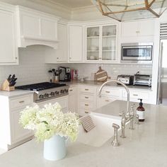 a large kitchen with white cabinets and marble counter tops is pictured in this image, the center island has a vase full of flowers on it