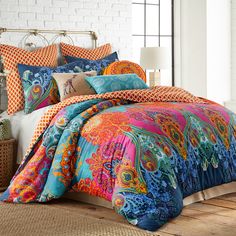 a bed with colorful comforters and pillows on top of wooden floor next to white brick wall