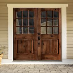 two wooden doors on the side of a house next to a brick walkway and potted plant