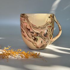 a coffee cup sitting on top of a table next to some dried yellow flowers and leaves