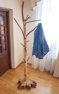 a coat rack is next to a tree in a room with wooden floors and windows