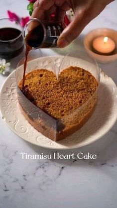 someone is pouring wine into a heart shaped cake on a plate with flowers and candles