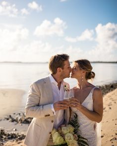 a bride and groom kissing on the beach