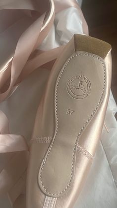 a pair of ballet shoes sitting on top of a white cloth covered floor next to a pink ribbon