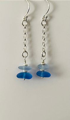 pair of blue glass beads dangling from silver earwires on white surface with metal chain