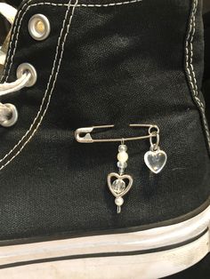 a pair of black sneakers with silver heart charms on the bottom and an ear pin attached to them