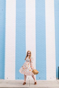 a woman standing in front of a blue and white striped wall holding a brown bag