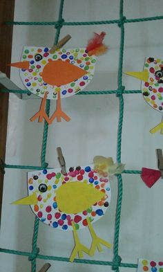 some paper birds are hanging on a green wire fence with pegs and colored dots