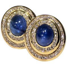 A pair of 14K yellow gold earrings centered around oval, cabochon, cut sapphires measuring 10mm X 12mm. Surrounding each sapphire, are two elliptical channels set with round brilliant cut diamonds. These modern earrings are set with a total of 2 sapphires weighing a total approximate weight of 14.25ct and 118 diamonds weighing a total of approximately 3.25ct. Signed Niva, they measure 1 inch long and 7/8 of an inch wide. Overall weight is 31.4 grams. Round Sapphire, Yellow Gold Earrings, Oval Earring, Yellow Gold Earring, Modern Earrings, Baguette Diamond, Emerald Diamond, Oval Diamond, Oval Cabochon