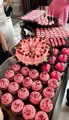 a table topped with lots of cupcakes covered in pink frosting