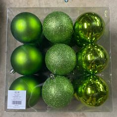 green and gold ornaments are in a clear box on the floor with a price tag