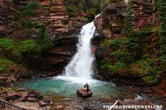 a person sitting on a rock in front of a waterfall