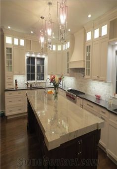 a large kitchen with marble counter tops and white cabinets, along with an island in the middle