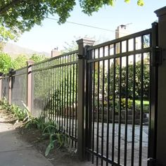 an iron fence is shown in front of a house with trees and bushes on the sidewalk