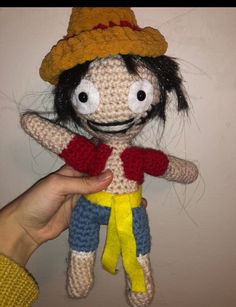 a crocheted doll is being held up by someone's hand and wearing a hat