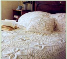 a white crocheted bedspread on top of a bed with two pillows