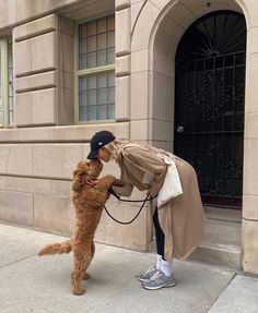 a woman is petting a dog on the side of the street in front of a building