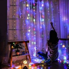 a person sitting on the floor in front of a window with lights all over it