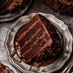 a slice of chocolate cake sitting on top of a silver plate next to two forks