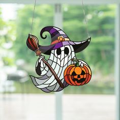 a stained glass hanging decoration with a witch holding a broom and pumpkin on it's head