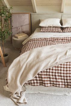 a bed with brown and white checkered comforter on it's side, next to a potted plant