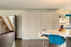 a kitchen with white counter tops and blue stools next to a spiral stair case