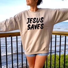 Jesus Saves Sweatshirt. This unisex Christian sweatshirt is versatile for many occasions. Share a simple Gospel message with a bold Jesus sweatshirt. This Jesus saves sweatshirt is soft in style but strong in faith. Wear it with leggings, or jeans, or jazz it up with your favorite Christian jewelry. It's a simple, bold faith sweatshirt that is sure to get attention wherever you may go. This world needs hope and a lot more Jesus. Wearing your faith with Christian clothing is a great way to spark Be The Light Sweatshirt, Jesus Has My Back Shirt, Christian Sweatshirts Cricut, Simple Gospel, Faith Crewneck, Matthew 1 21, Biblical Sweatshirts, Bold Faith, Faith Sweatshirt