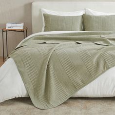 a bed covered in a green blanket and pillows next to a night stand with two nightstands