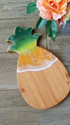 a wooden cutting board with a green frog on it next to an orange and pink flower