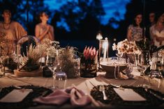 a group of people standing around a table with flowers and candles on it at night