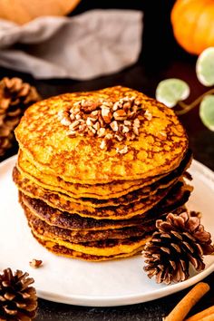 a stack of pancakes sitting on top of a white plate next to some pine cones