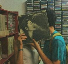 a man holding up a record in front of a book shelf with records on it