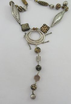 This is a fabulous sterling silver necklace with various ethnic tribal stone beads and large sterling silver woven beads. The central pendant is open and it has a long dangle attached to it. I believe the small beads are made out of bone. The beads are set in an almost symmetrical pattern starting from the central pendant and made out to resemble African necklaces. Probably artisan made. Very stylish and unique. The beauty of it all -- is the soft mellow chime that emanates from the round balls