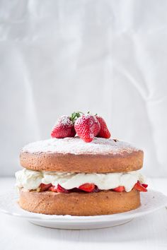 a white plate topped with a cake covered in frosting and strawberries on top of it