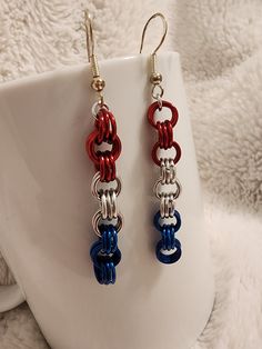 two red, white and blue earrings sitting on top of a white cup next to a mug