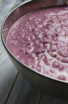 a metal bowl filled with purple liquid on top of a wooden table next to an orange slice