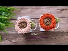 two coffee mugs with crocheted flowers on them