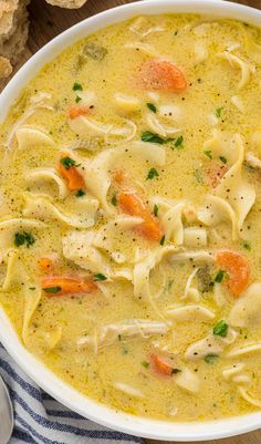 a white bowl filled with chicken noodle soup next to some bread on a table