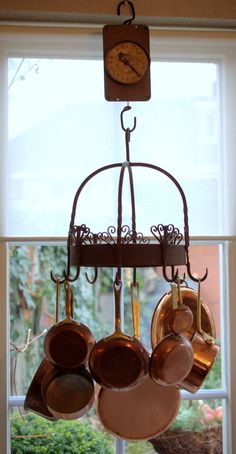 pots and pans hanging from a rack in front of a window with a clock