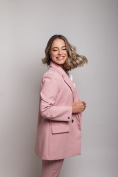 a woman in a pink suit posing for the camera with her hair blowing in the wind