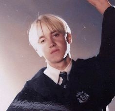 a young man with blonde hair wearing a black shirt and tie holding his hand up to the side