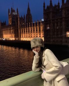 a woman wearing a white coat and hat standing in front of the palace of westminster