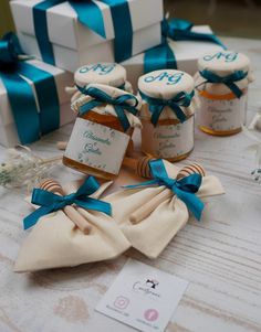 small honey jars with blue ribbons and tags are on the table next to gift boxes