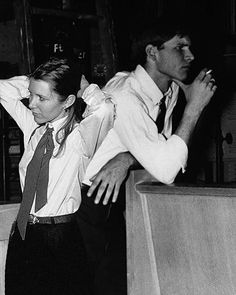 black and white photograph of two men standing next to each other with their hands in the air