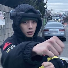 a young man in a hoodie pointing at something on the side of the road