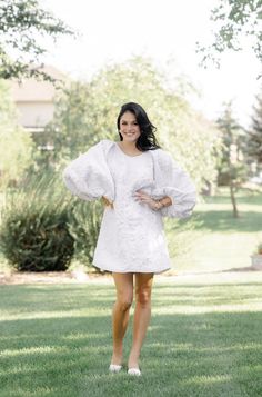 a woman standing in the grass wearing a white dress