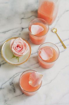 three glasses filled with rose lemonade on a marble counter top next to two spoons