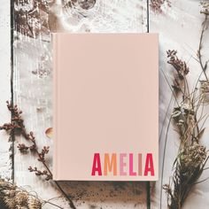 an open book with the word amella on it next to dried plants and flowers