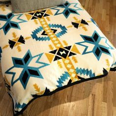 a bed with a blue and yellow blanket on top of it next to a pillow